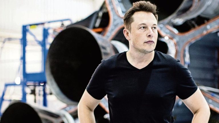 Elon Musk Standing In a black t-shirt in spacex factory infront of a falcon engine exhaust nozzles - 8 books that inspired elon musk into starting tesla, spacex, boring company etc.